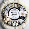 Baby announcement new years with teddy bear, shoes, onesie, and ultrasound photo on a fluffy white background.
