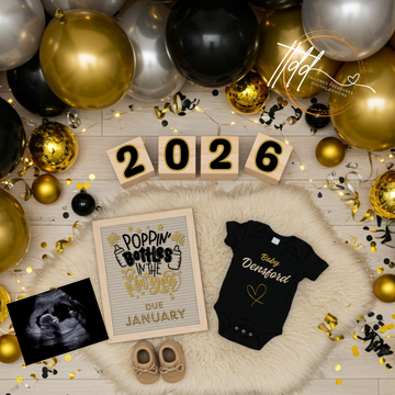 New Year's Baby Reveal with balloons, baby onesie, and ultrasound photo on a wooden surface.